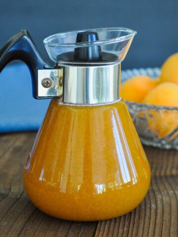 a dispenser of fresh made syrup in front of a bowl of apricots