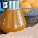 A glass pitcher of apricot syrup sits in front of a bowl of fresh apricots on a wooden table, capturing the sweet essence of homemade apricot syrup.