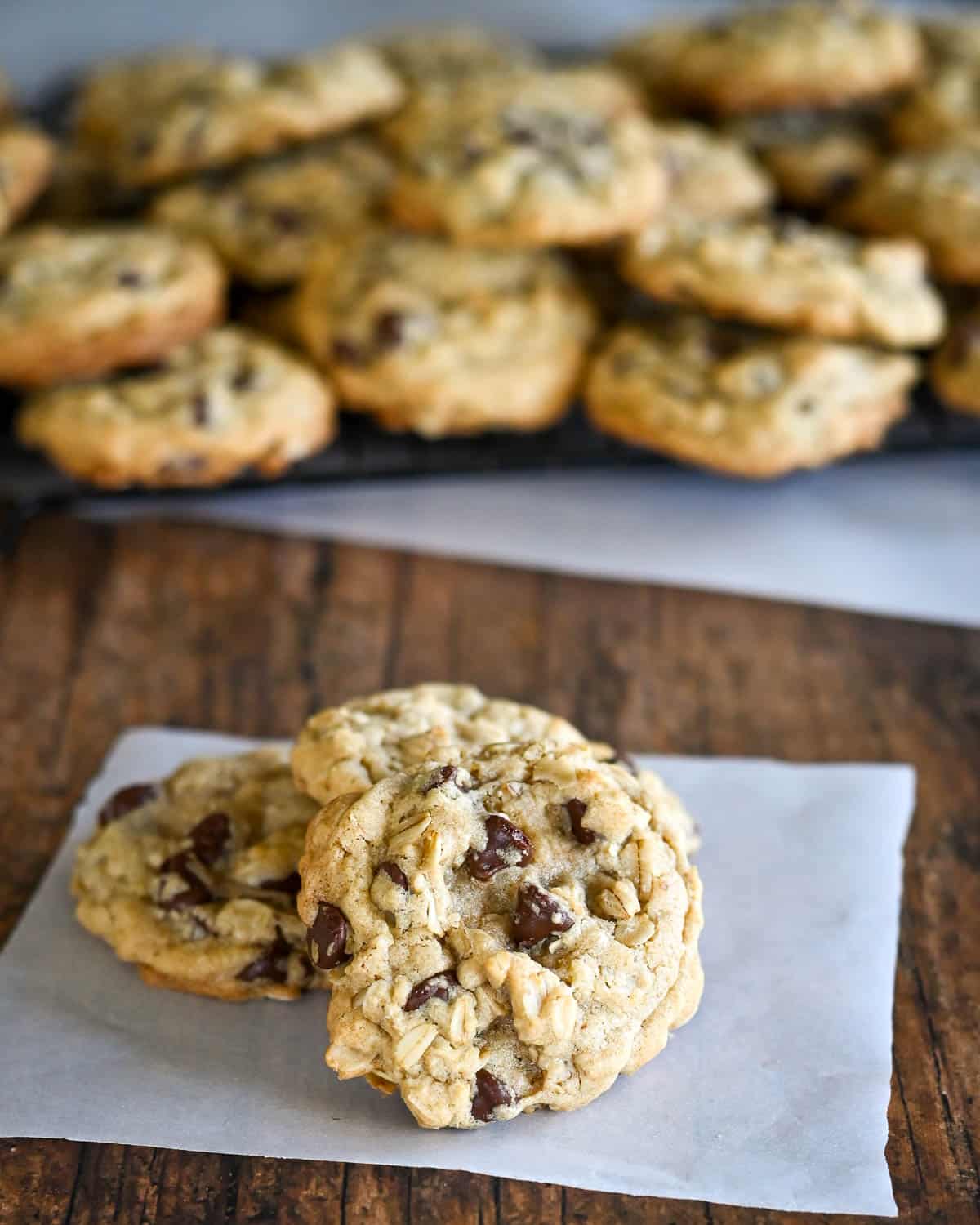 A few cookies on parchment paper in front of a rack of cooling cookies. 