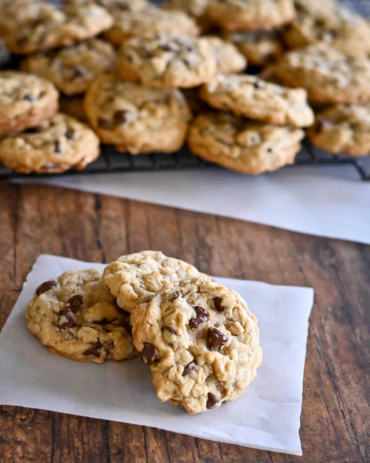 A few cookies on parchment paper in front of a rack of cooling cookies.