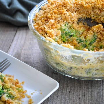 a casserole made with broccoli and cheese in a clear dish next to a white plate