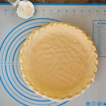 Pie dough in a pie plate next to flour on a pastry mat.