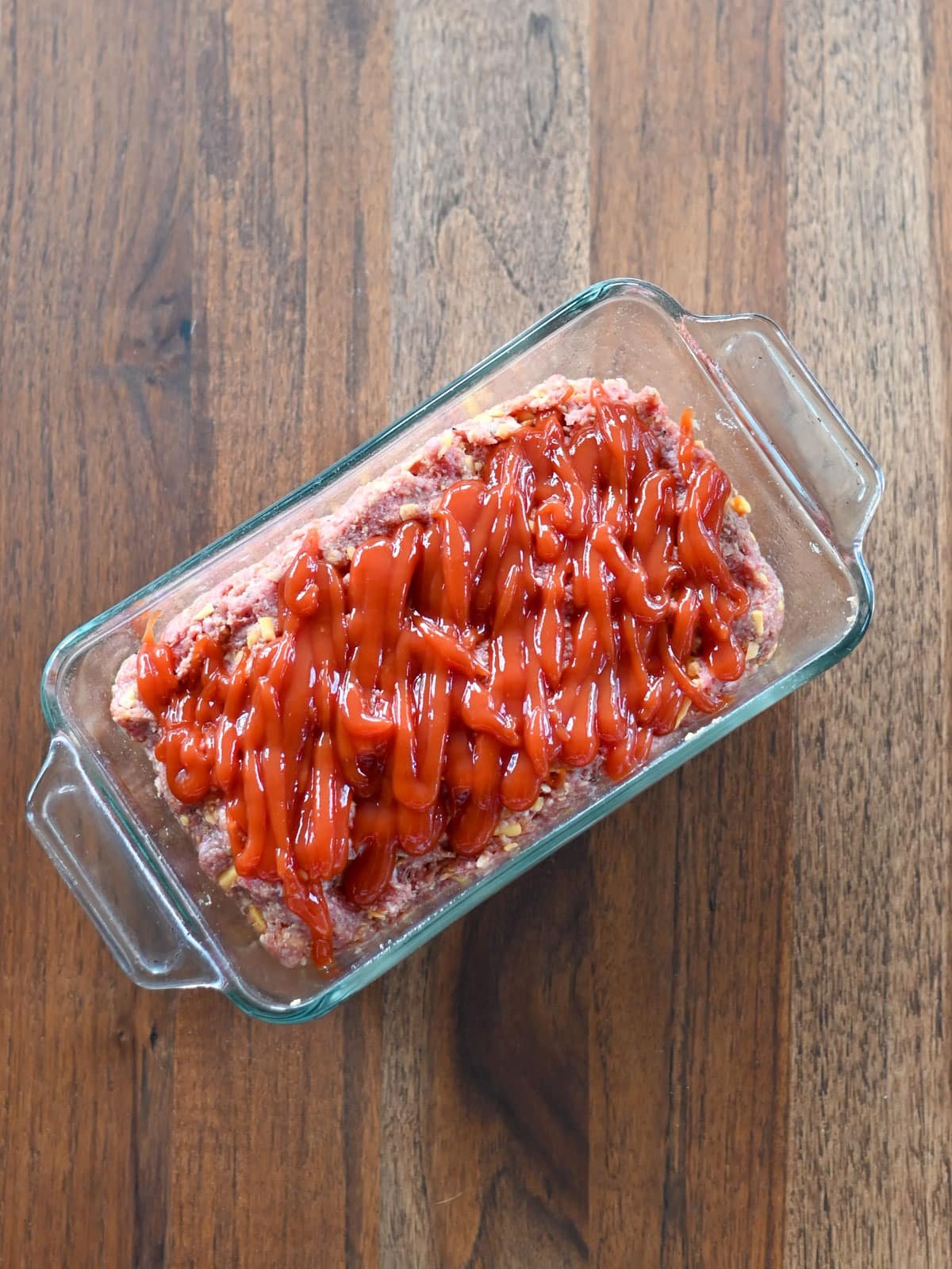 Raw meatloaf topped with ketchup in a baking dish. 
