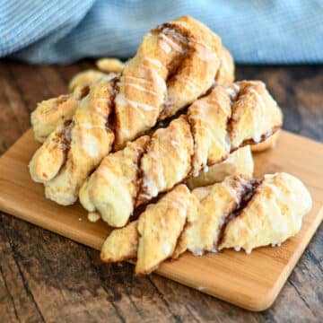 Baked cinnamon twists on a wood board next to a blue towel.