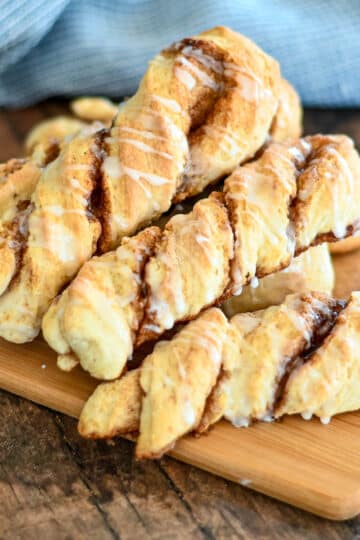 Baked cinnamon twists on a wood board next to a blue towel.