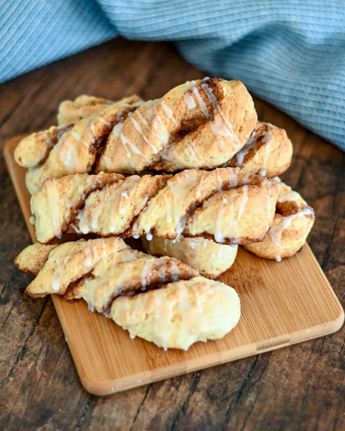 Baked cinnamon twists on a wood board next to a blue towel. 