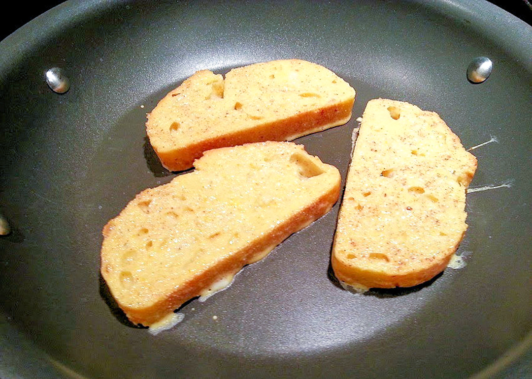 3 slices of french toast cooking in a skillet