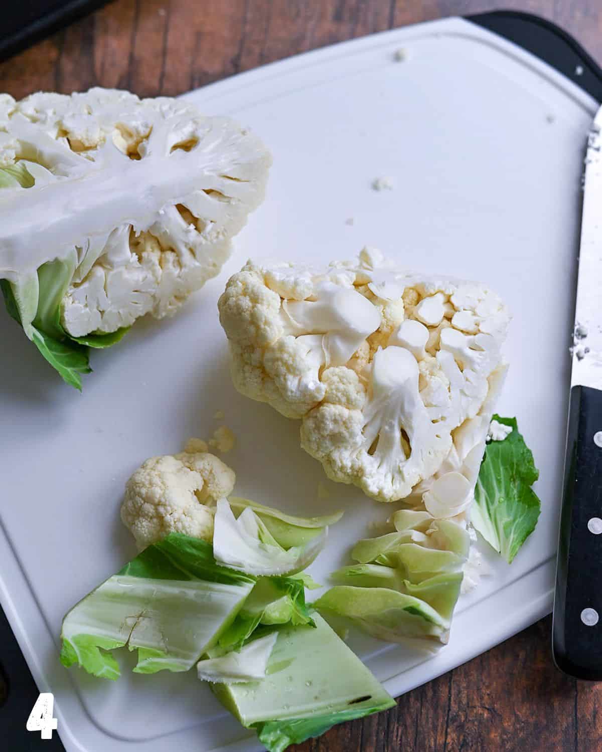 A white cutting board with a knife and chopped cauliflower.