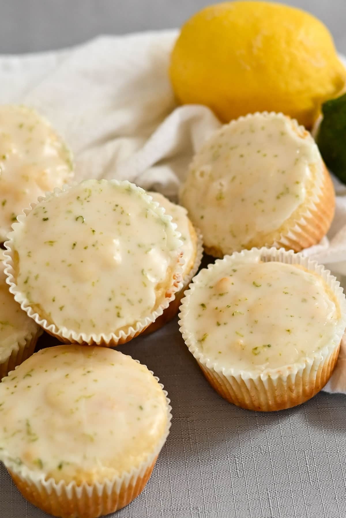 Lemon-lime glazed muffins, reminiscent of Lemon Lime Muffins, on a gray surface with a lemon and a lime in the background.