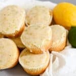 Lemon Lime Muffins glazed with citrusy zest are stacked on a white cloth, accompanied by fresh lemon and lime for a burst of flavor and color.