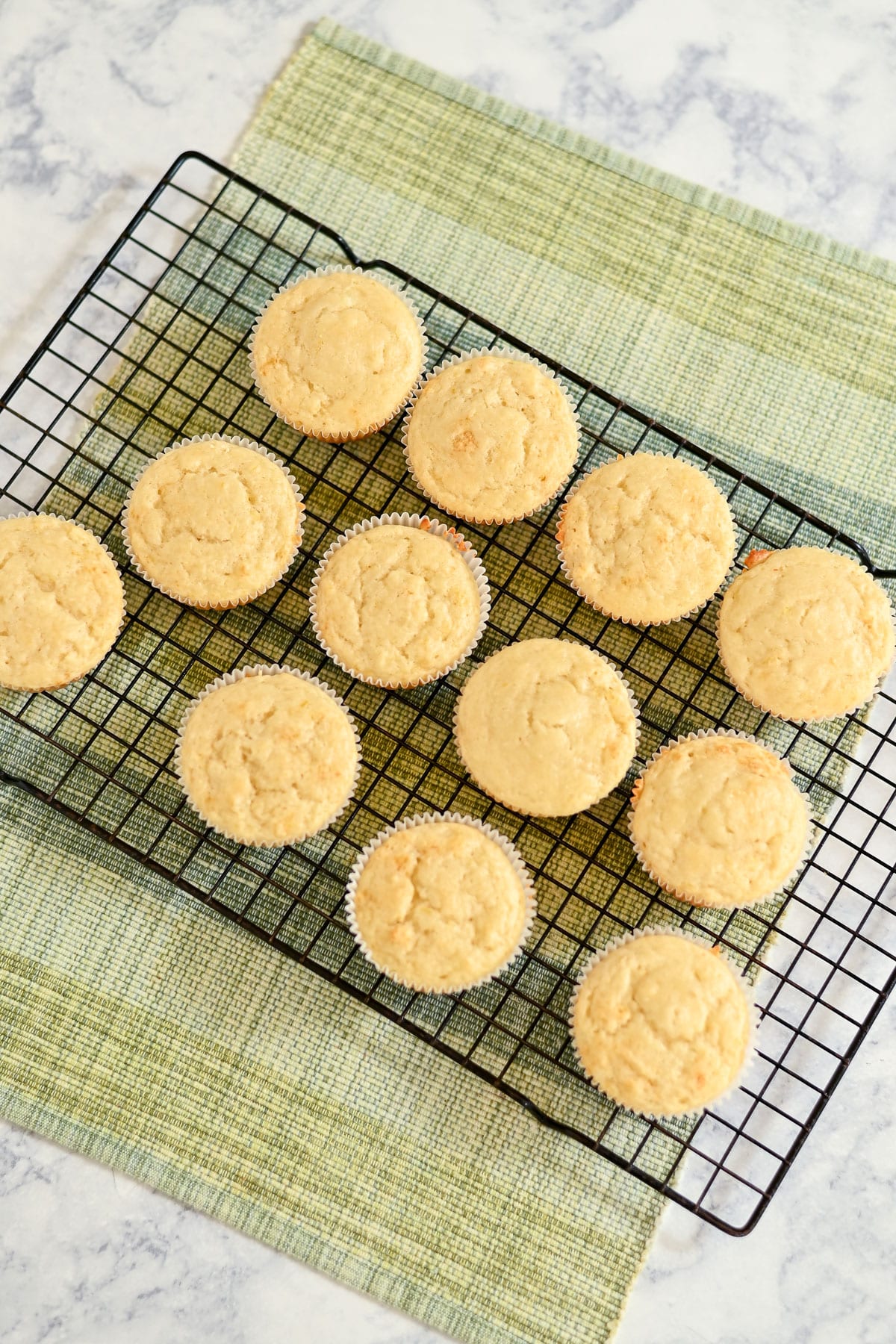 Lemon Lime Muffins cooling on a black wire rack over a green placemat on a marble surface.