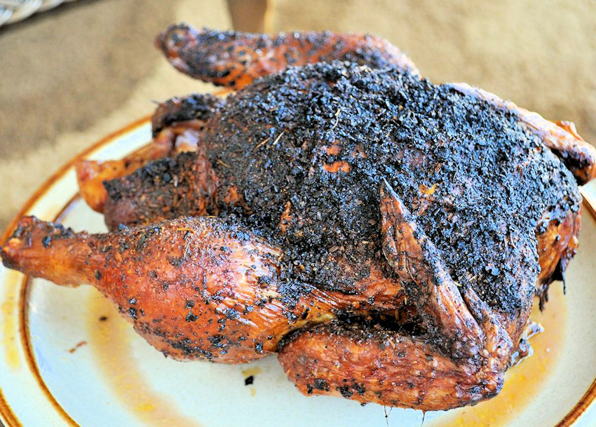 a slightly charred, whole chicken that has been cooked on a bbq