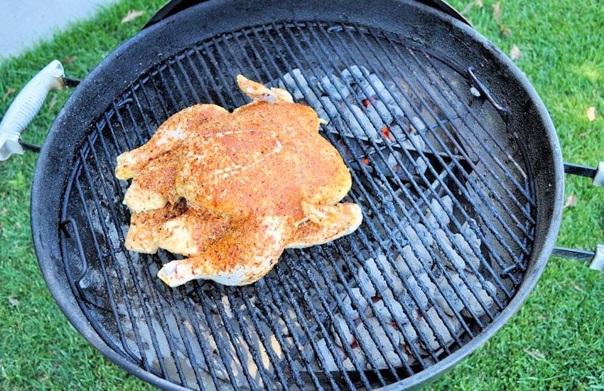 a raw chicken coated in seasoning starting to cook on a weber bbq