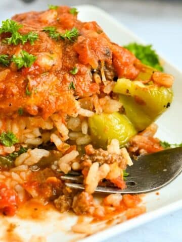 A delicious stuffed bell pepper filled with rice and ground beef, topped with tomato sauce and parsley, sits enticingly on a white plate with a fork.