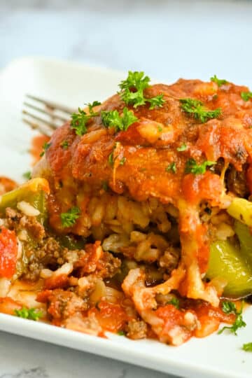 Stuffed Bell Peppers with meat, rice, and tomato sauce garnished with parsley on a white plate with a fork.