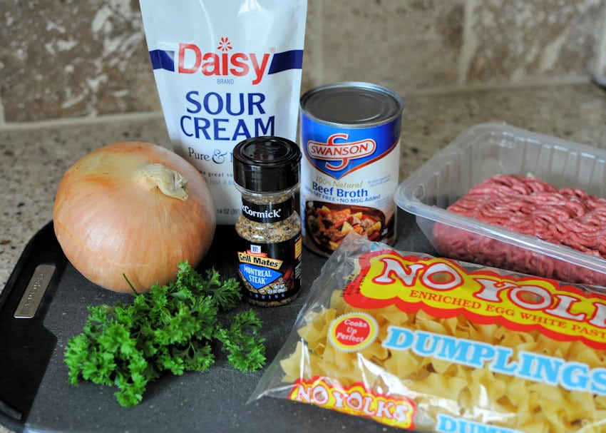 sour cream, beef broth, montreal seasoning, onion, noodles, ground beef, parsley setting on a black cutting board