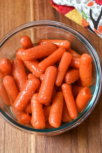Glazed carrots in a clear glass bowl next to a kitchen towel.