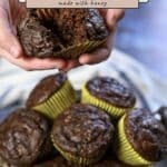 Hands holding a delicious Chocolate Banana Muffin over a basket filled with more chocolate banana muffins in yellow wrappers.