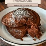 Three easy chocolate pancakes with cocoa powder dusted with powdered sugar on a plate, with a fork holding a bite-sized piece.