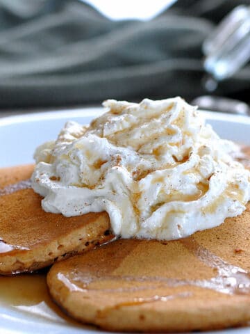 pancakes on a white plate topped with whipped cream