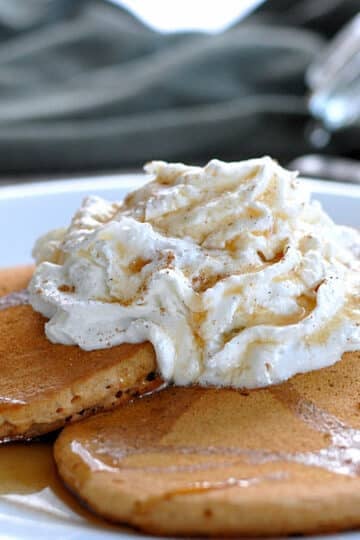 pancakes on a white plate topped with whipped cream