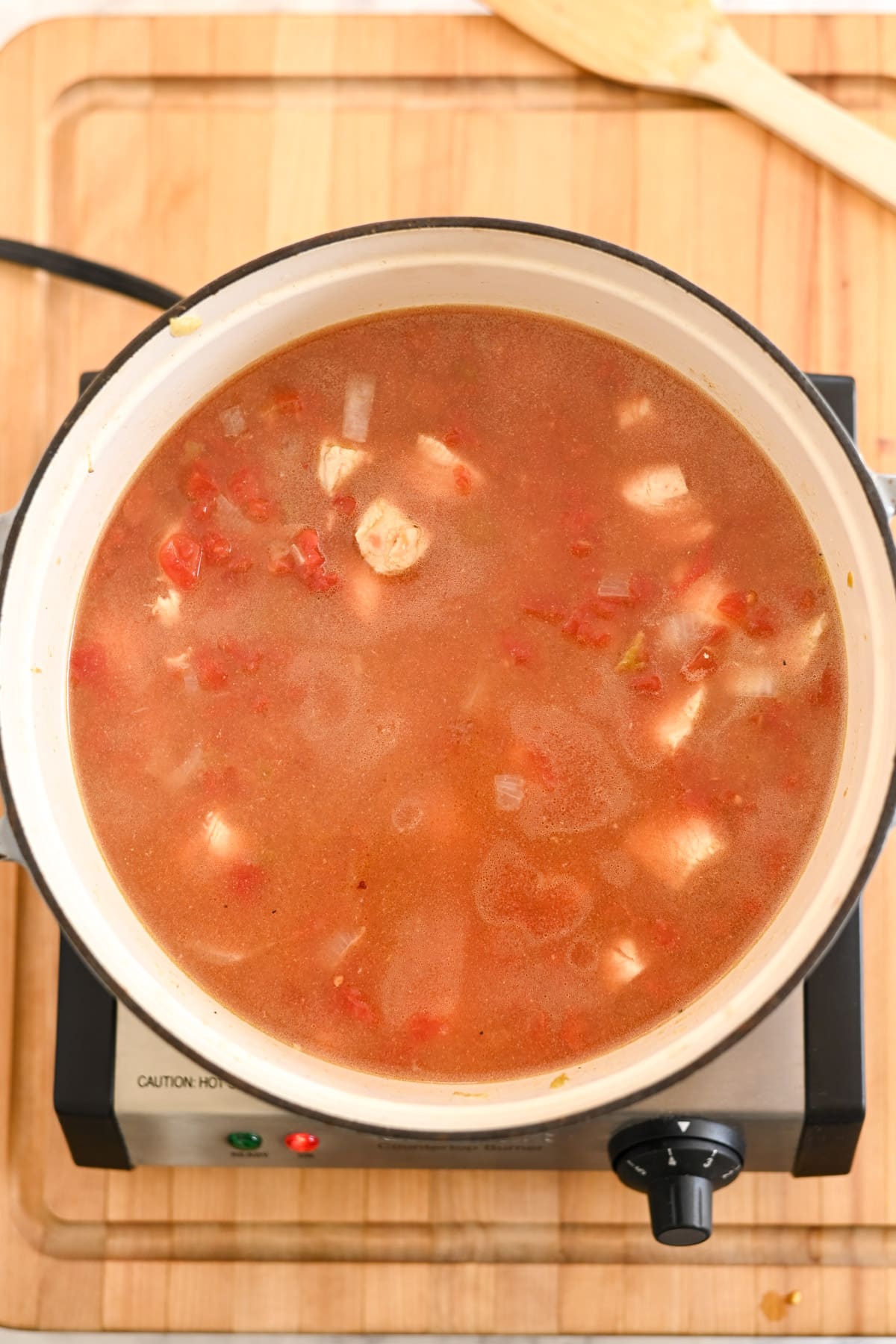 A pot of Mexican Chicken Soup with chunks of vegetables and meat simmers on an electric stove atop a wooden surface.