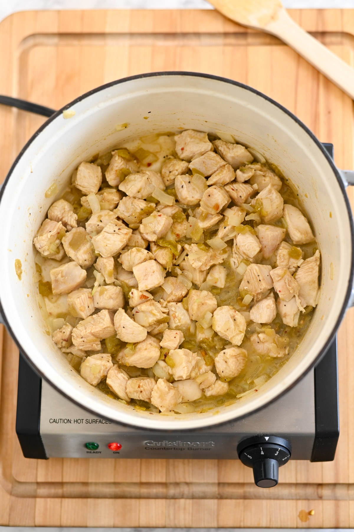 A pot of diced chicken is simmering on the stovetop, infused with Mexican Chicken Soup seasonings, all resting invitingly on a rustic wooden surface.