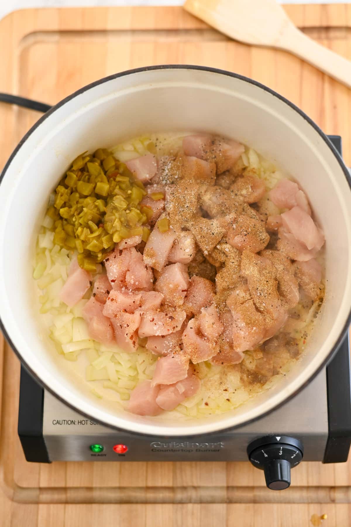 Chopped chicken, onions, and green peppers simmer together in a pot on the burner with seasoning sprinkled on top.