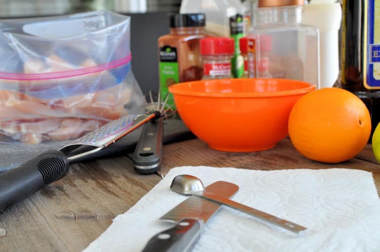 an orange, spices, a bowl, and utensils for prepping to prepare a citrus marinade for chicken fajitas