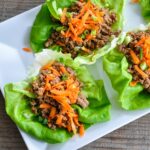 ground meat sitting in a lettuce cup with shredded carrots