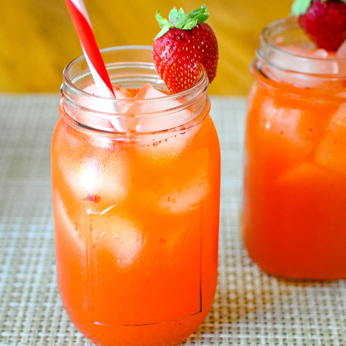 strawberry lemonade in a mason jar glass with ice and a red and white straw