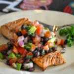 salmon filet covered with black bean salsa on a cream colored plate