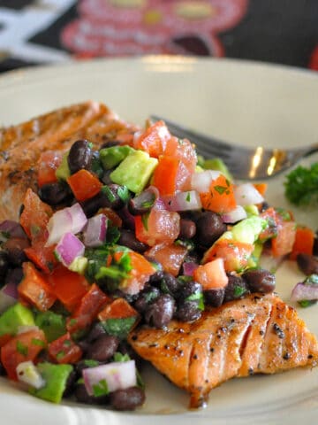 salmon filet covered with black bean salsa on a cream colored plate
