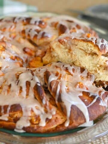 A glazed Peach Cinnamon Twist pull-apart bread on a glass plate, with one piece being pulled out, showcasing its soft, fluffy texture.