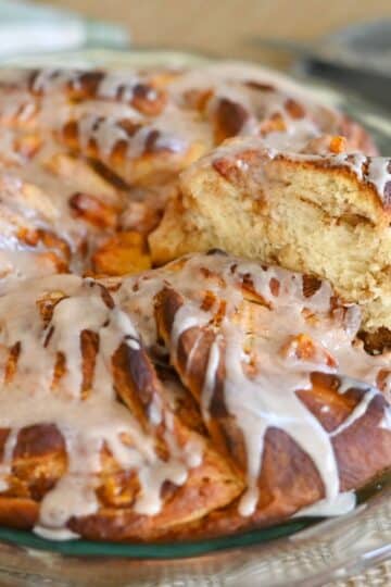 A glazed Peach Cinnamon Twist pull-apart bread on a glass plate, with one piece being pulled out, showcasing its soft, fluffy texture.