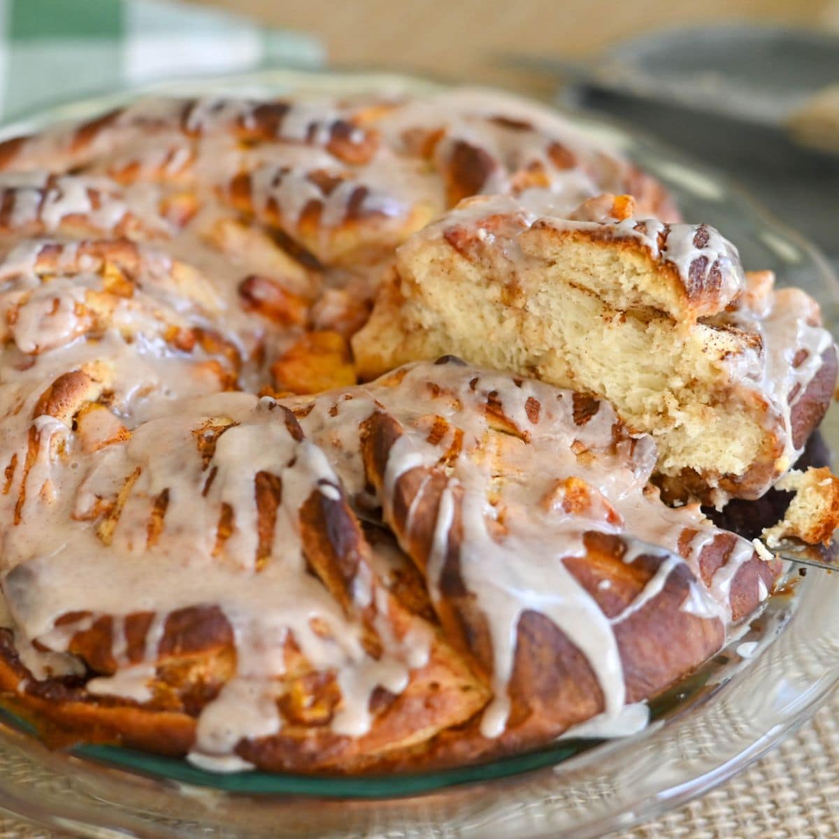 A glazed Peach Cinnamon Twist pull-apart bread on a glass plate, with one piece being pulled out, showcasing its soft, fluffy texture.