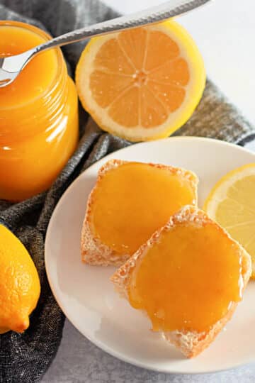 A jar of homemade lemon curd next to a plate with toast and lemons.