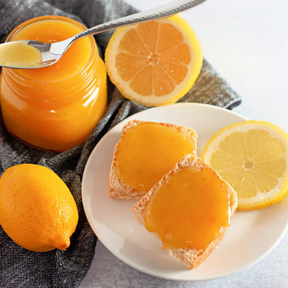 A jar of homemade lemon curd next to a plate with toast and lemons.