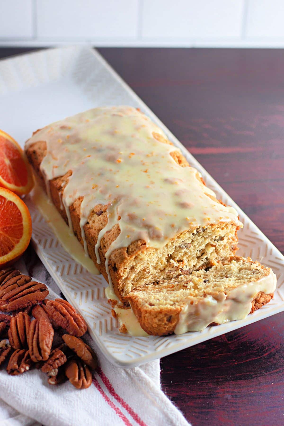 Glazed orange bread on a white platter next to cut oranges.