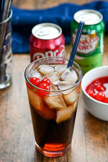 Soda with cherries next to a blue towel and a glass of straws.