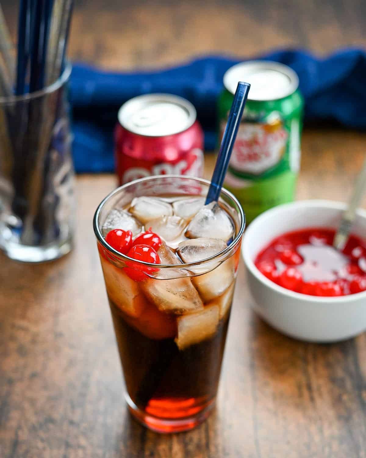 A Dr. Pepper beverage in a glass with ice topped with maraschino cherries. 