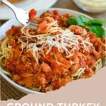 A plate of spaghetti topped with Ground Turkey Spaghetti Sauce and grated cheese, with a fork and side dishes visible.