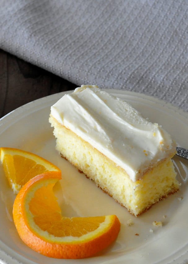 a slice of orange cake next to an orange slice on a beige plate