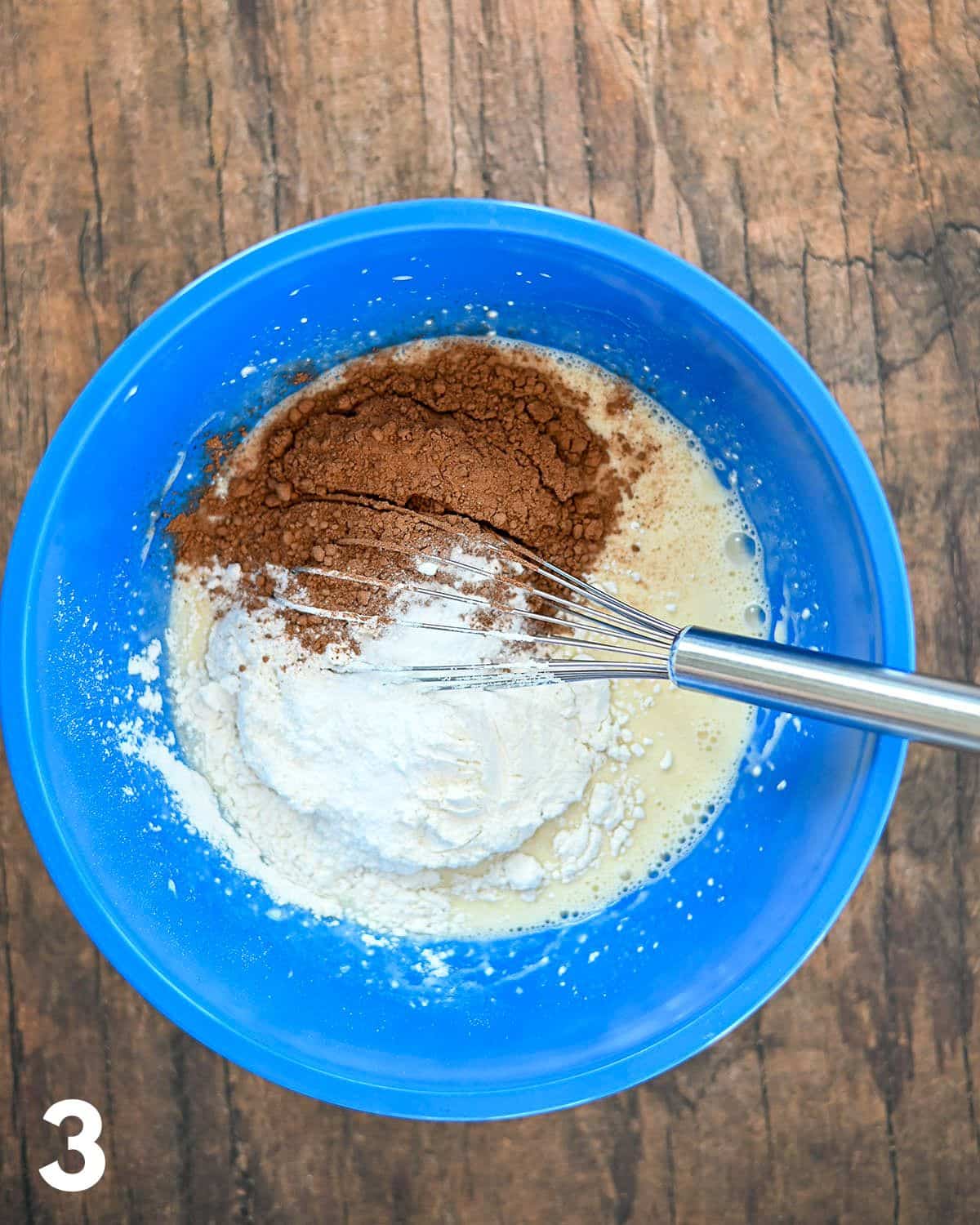 Flour and cocoa powder being added to liquid ingredients in a blue bowl.