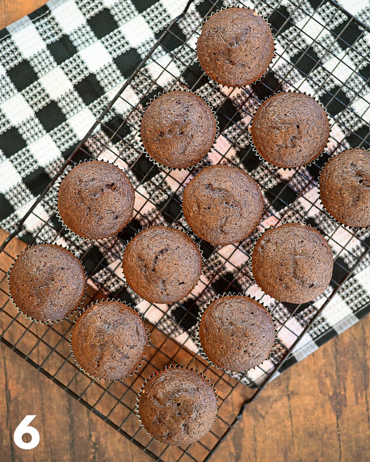 Just baked chocolate cupcakes on a rack over a checkered towel.