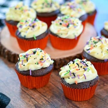 Chocolate cupcakes with buttercream frosting and sprinkles on a brown table.