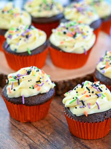 Chocolate cupcakes with buttercream frosting and sprinkles on a brown table.