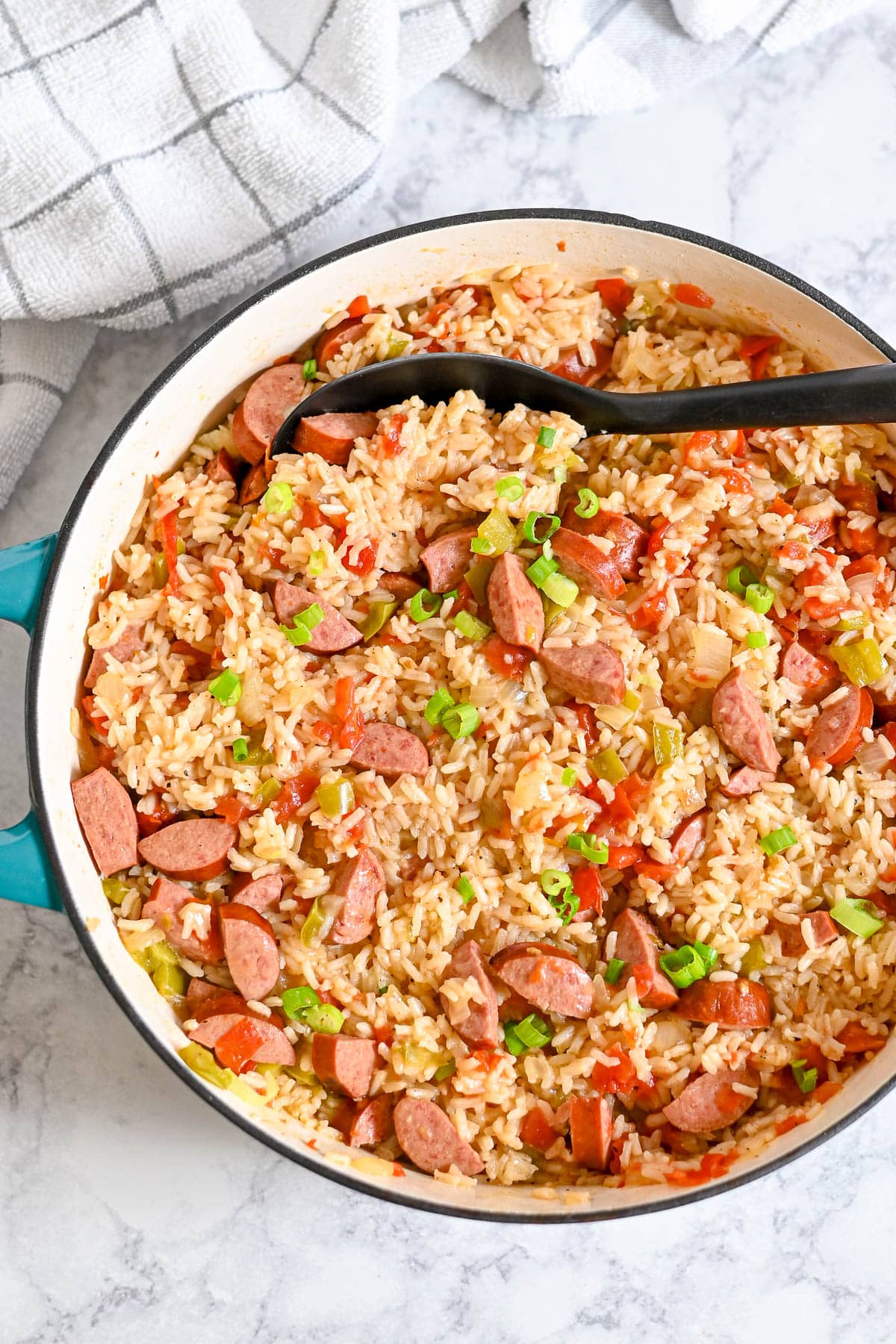 A pot of smoked sausage jambalaya with rice, vegetables, and sliced sausage, topped with chopped green onions.