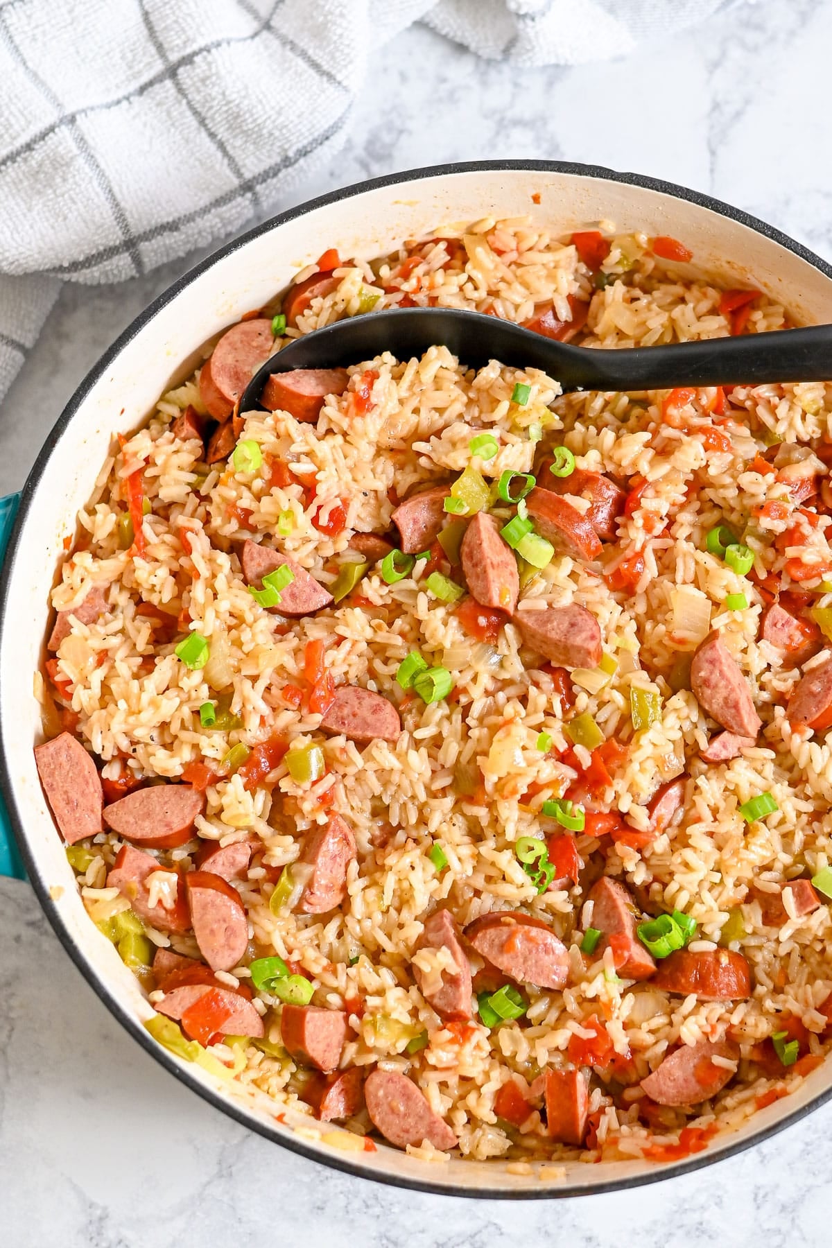 A pot of Smoked Sausage Jambalaya with rice, bell peppers, tomatoes, and green onions.