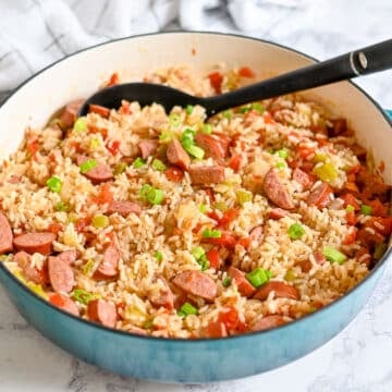 A skillet filled with sausage and rice, mixed with bell peppers and topped with chopped green onions.